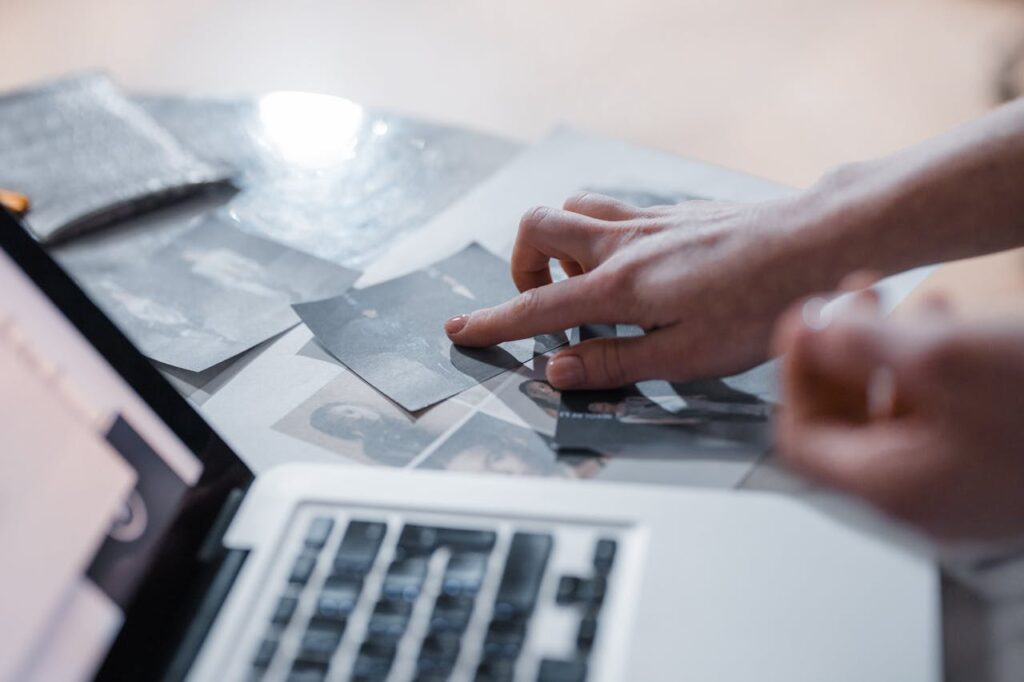 A hand arranges vintage photographs near a laptop in a modern workspace.